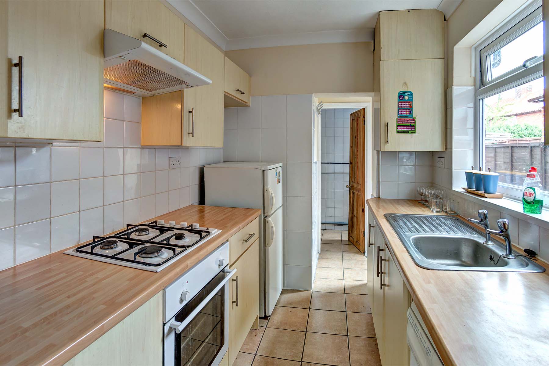Galley kitchen with wood effect worktops, cream cabinets, and white goods