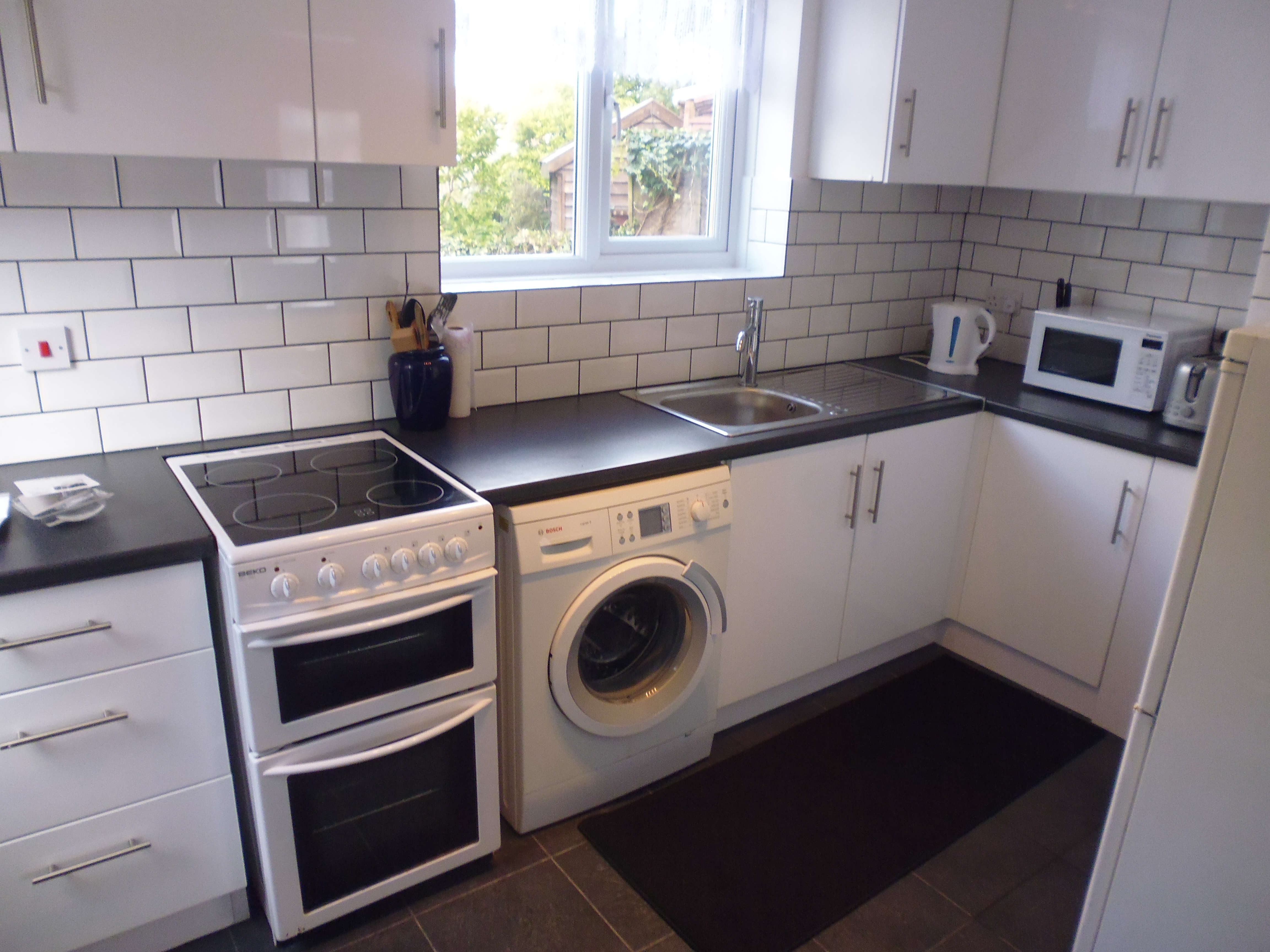 Kitchen with white cabinets, black worktop, and white goods.