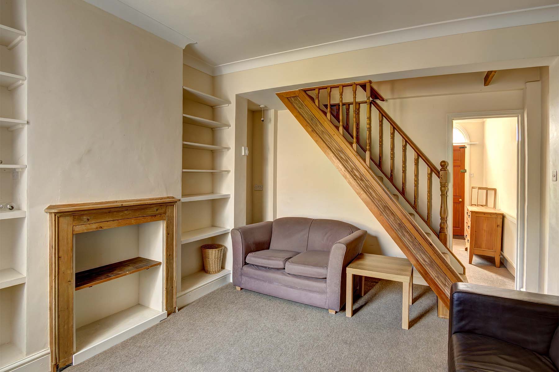 Lounge area with a fabric sofa under the stairs, a brown carpet, built in shelving on feature wall. A brown leather sofa also in the lounge area.