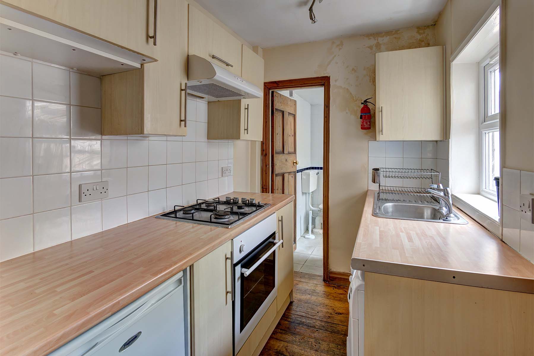 Galley style kitchen with wooden cupboards and worktop. Under the counter fridge, oven and washing machine.