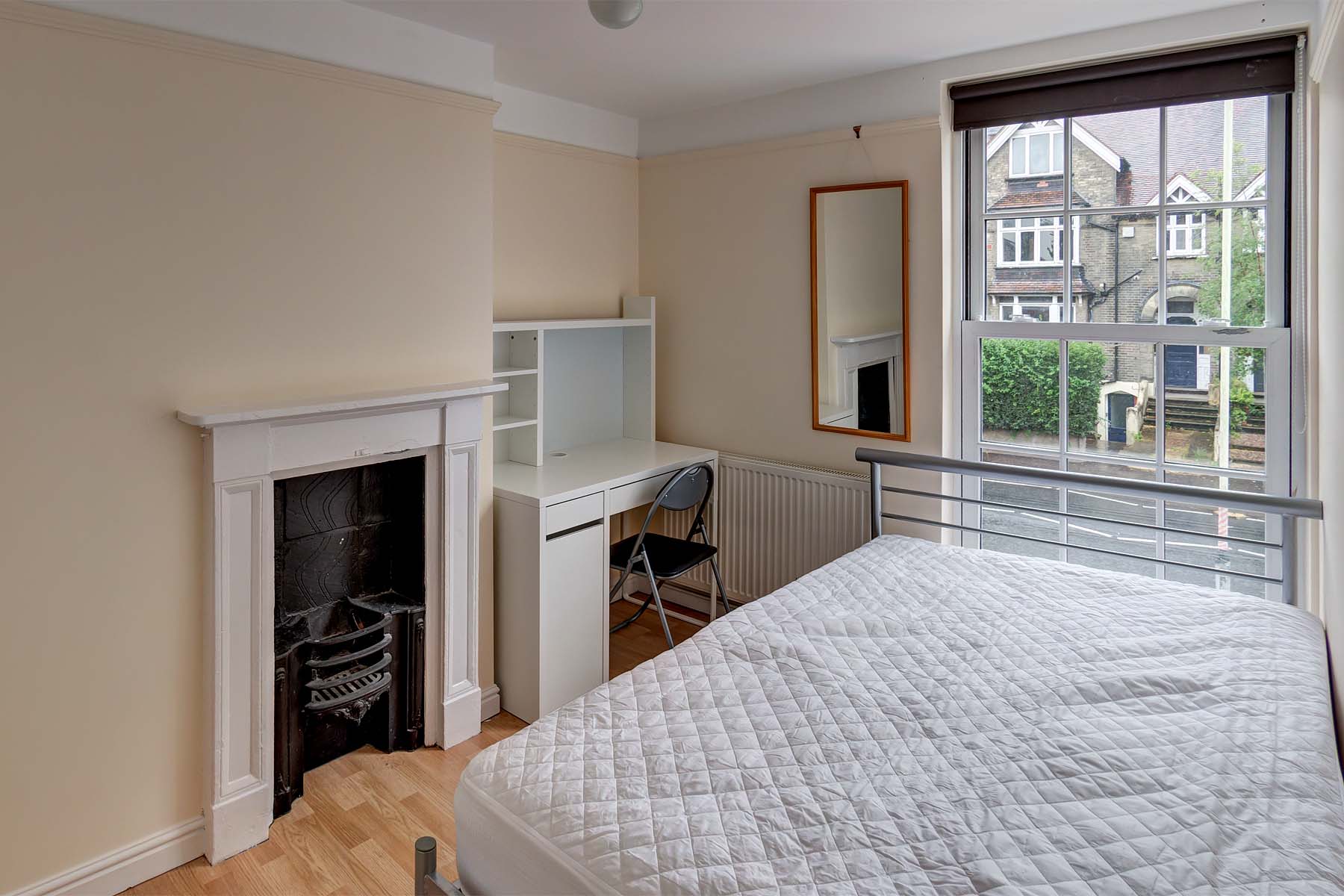 Double bedroom with magnolia walls, a metal double bedframe, a white desk and a mirror on the wall.