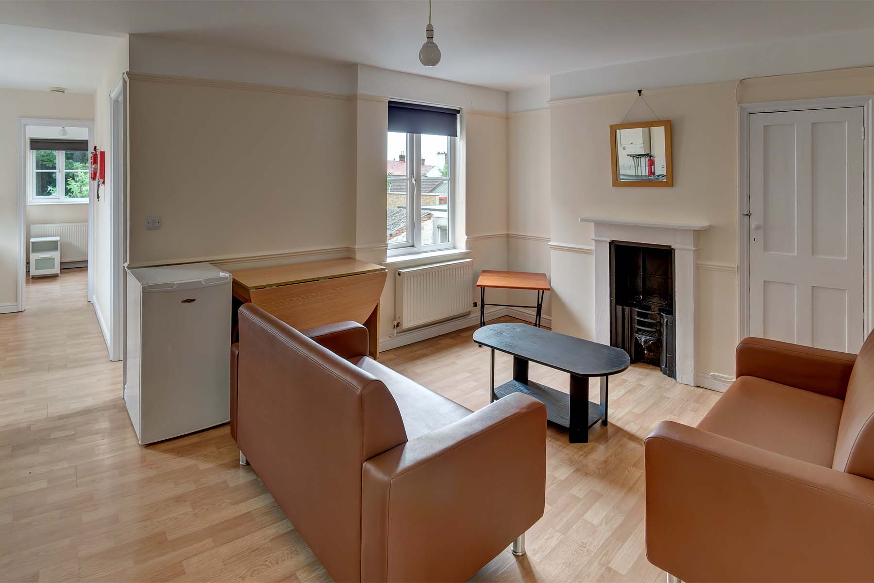 Lounge area with lino flooring, two brown leather sofas a black coffee table and decorative fireplace.