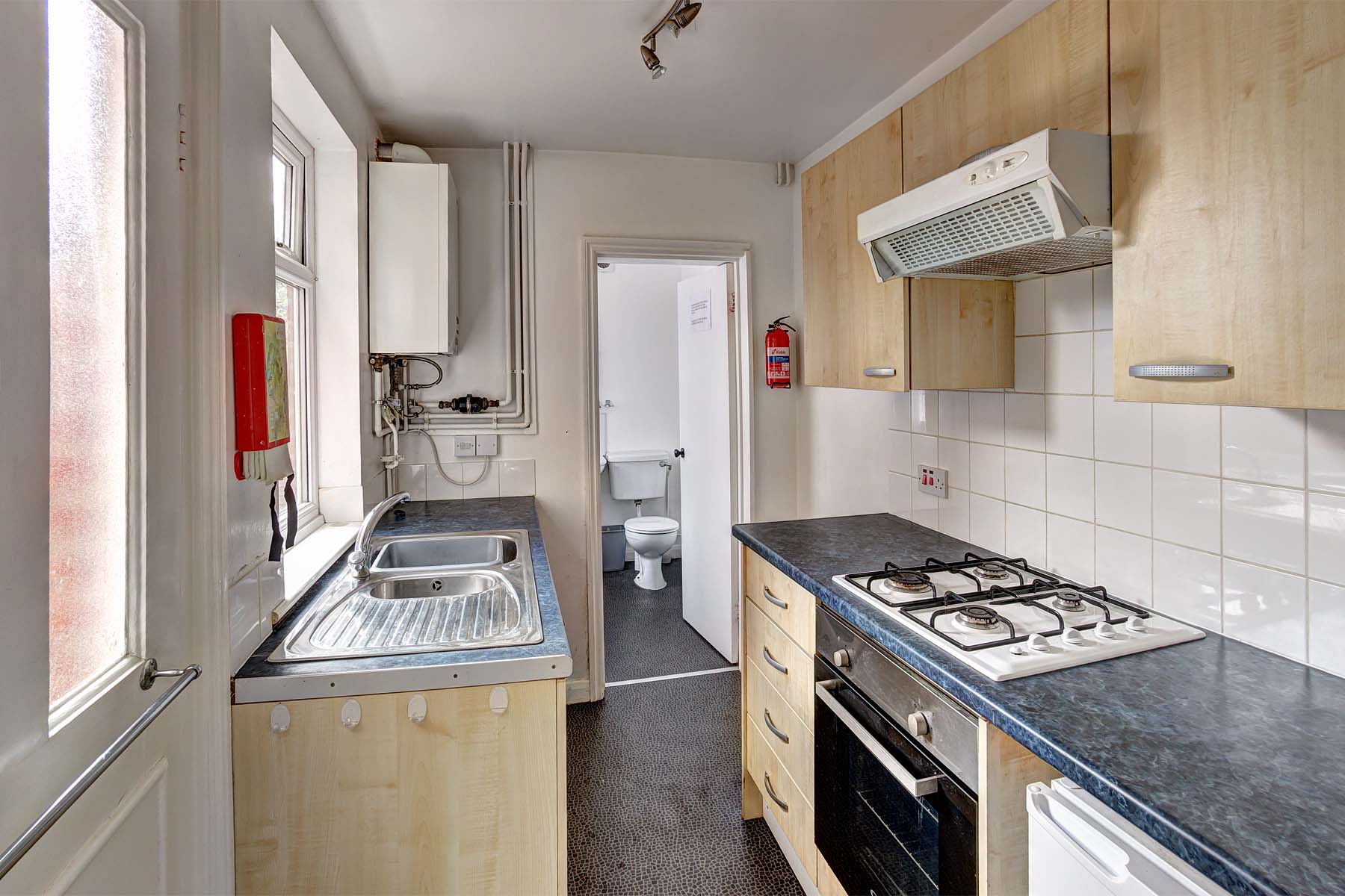 Galley kitchen with wood effect cupboards, black worktops, and white goods. Leading to bathroom