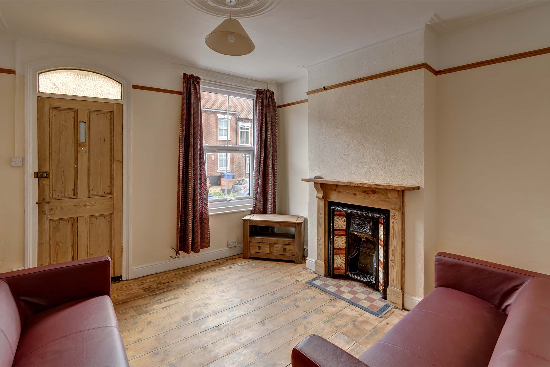 Lounge area with two dark red leather sofas, wooden flooring, wooden front door and a wooden decorative fireplace.