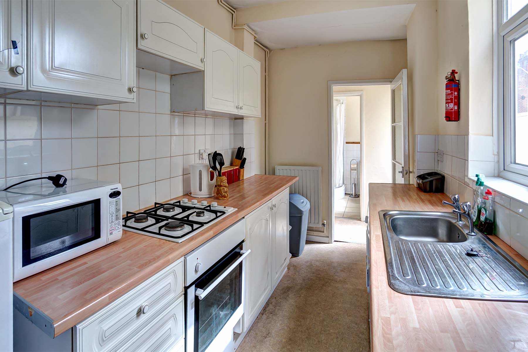 Modern galley kitchen with white cabinets and wood effect work top, and white goods.