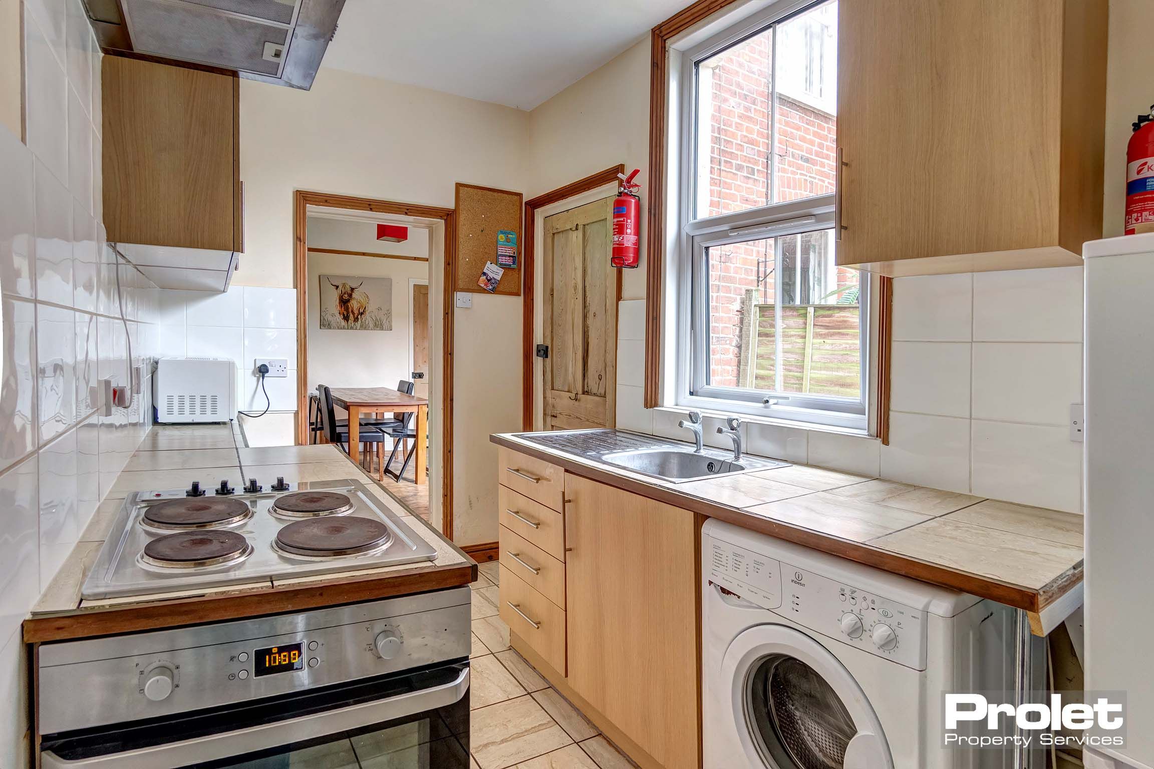 Galley style kitchen with wood effect fitted units, a washing machine, oven/hob and extractor fan.