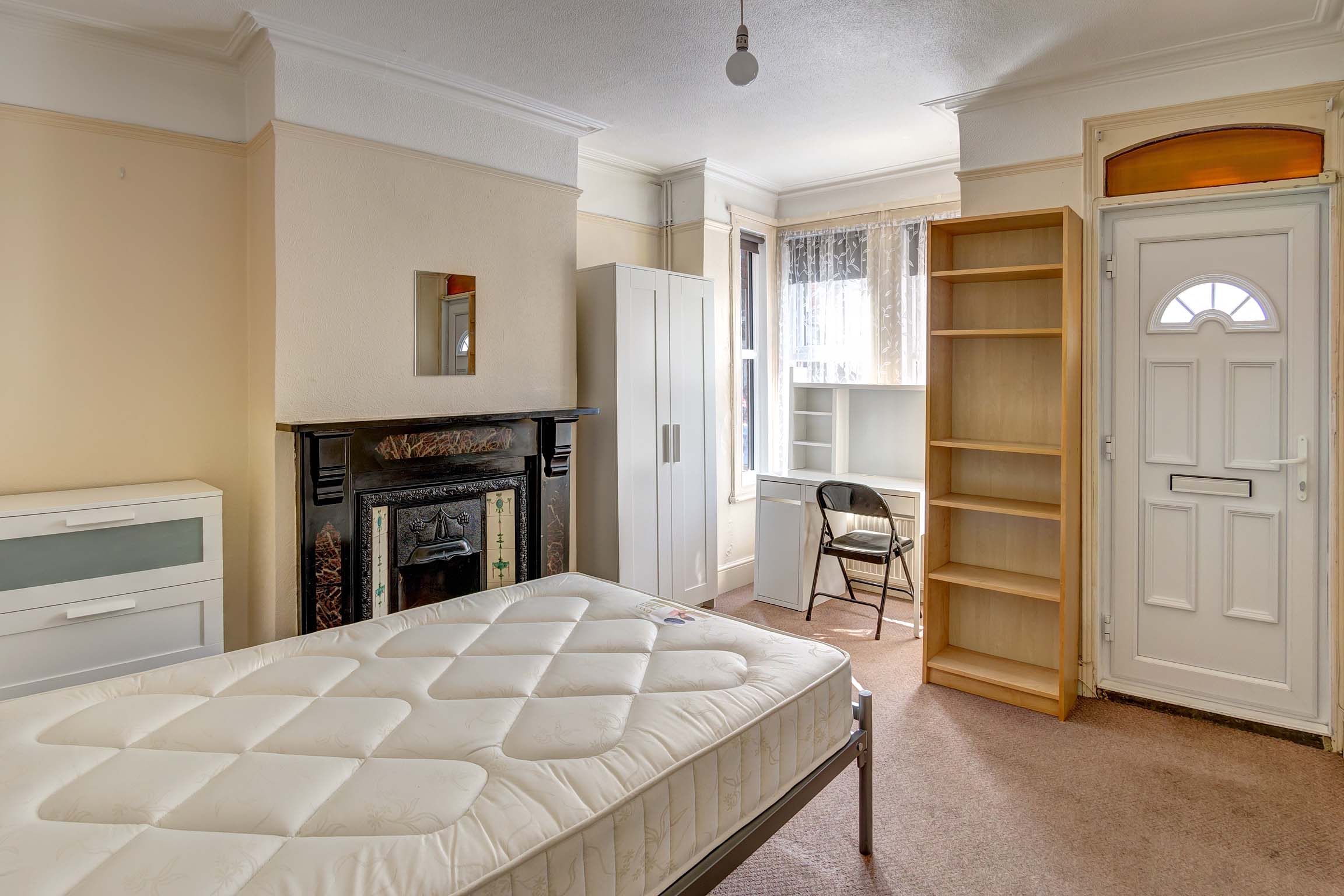 Bedroom with front door access, a decorative fireplace. White wardrobe, chest of drawers and desk.