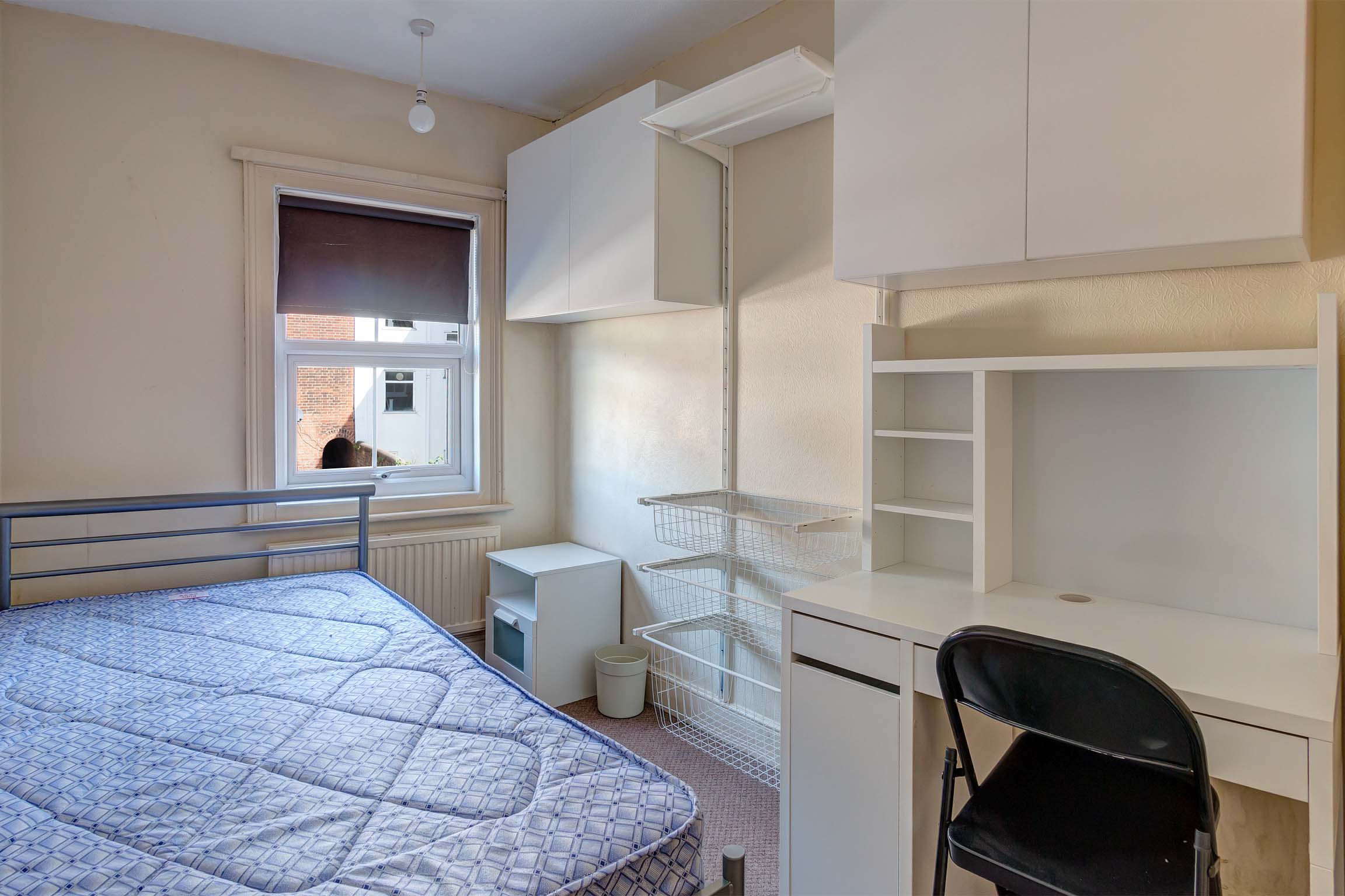 Bedroom with double bed, fitted storage space on one wall including a desk and a chair.
