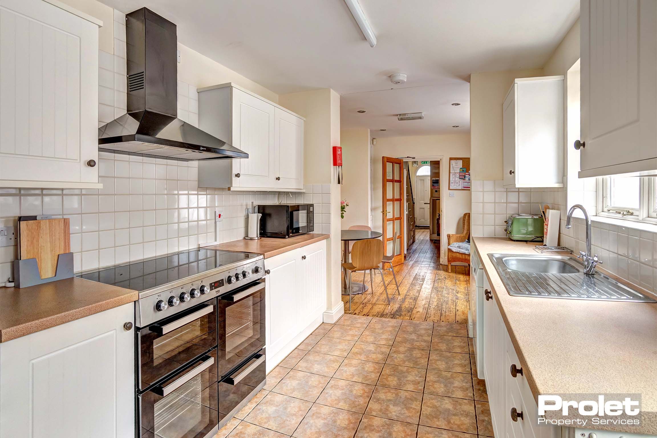 Large galley style kitchen with wood floors and white units, leading into dining room