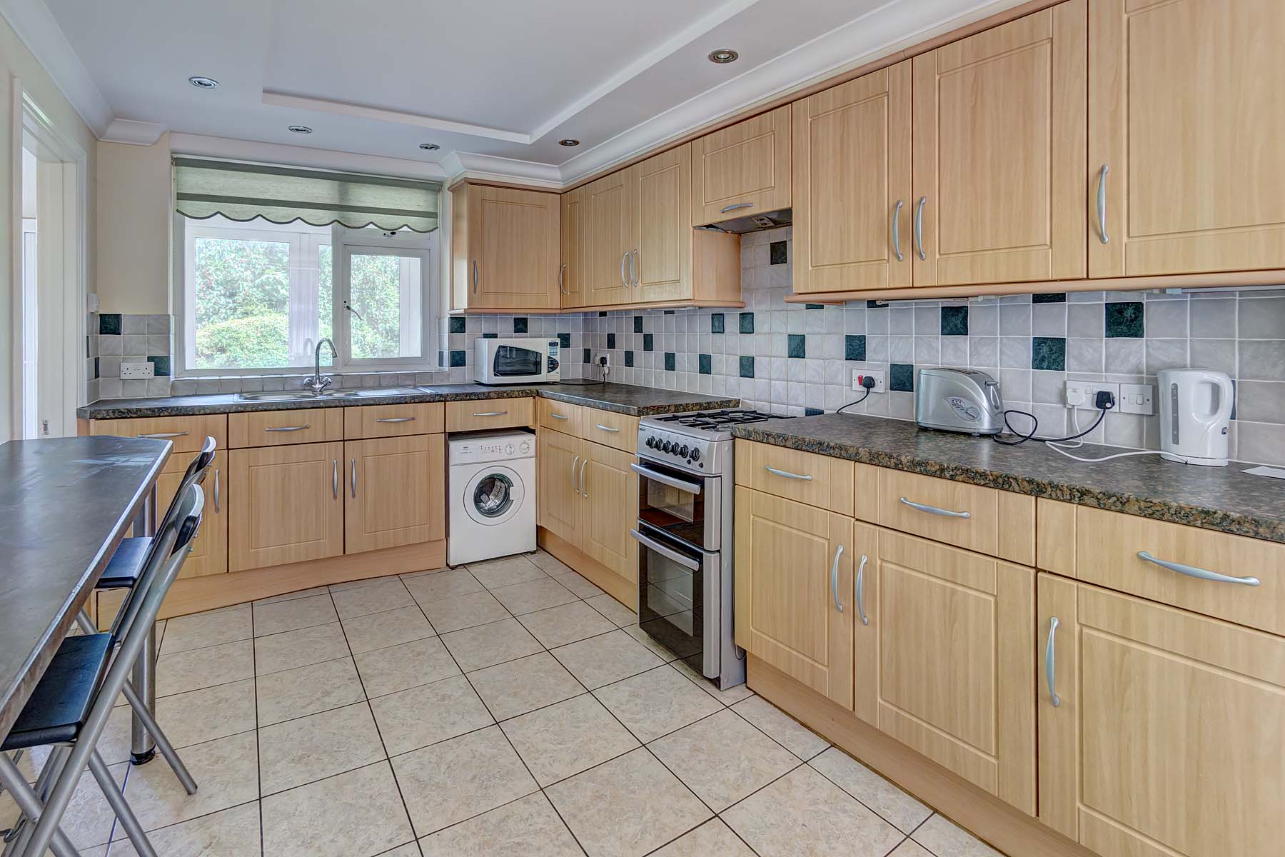 Large kitchen with wooden cabinets, black worktop, and tiled floor