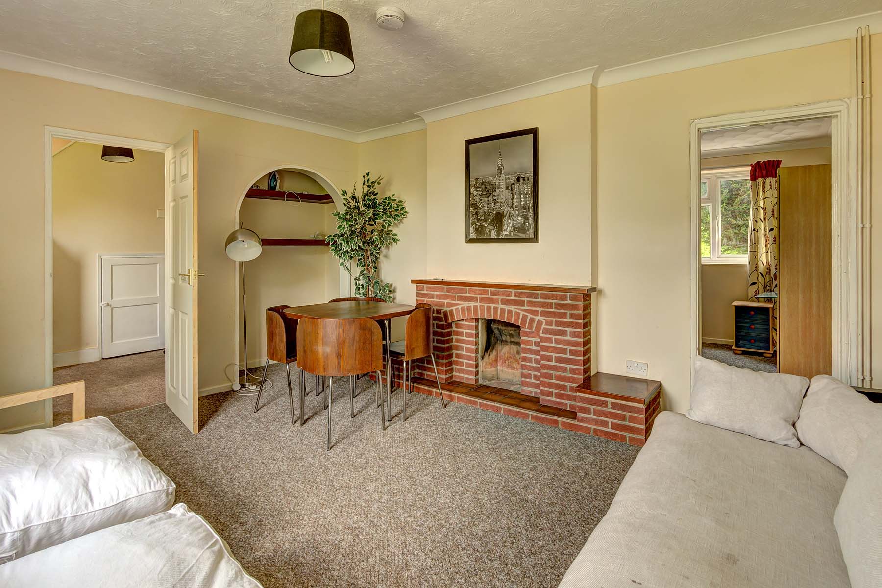 Lounge space with magnolia painted walls. A red brick decorative fire place and a wooden look dining table set.