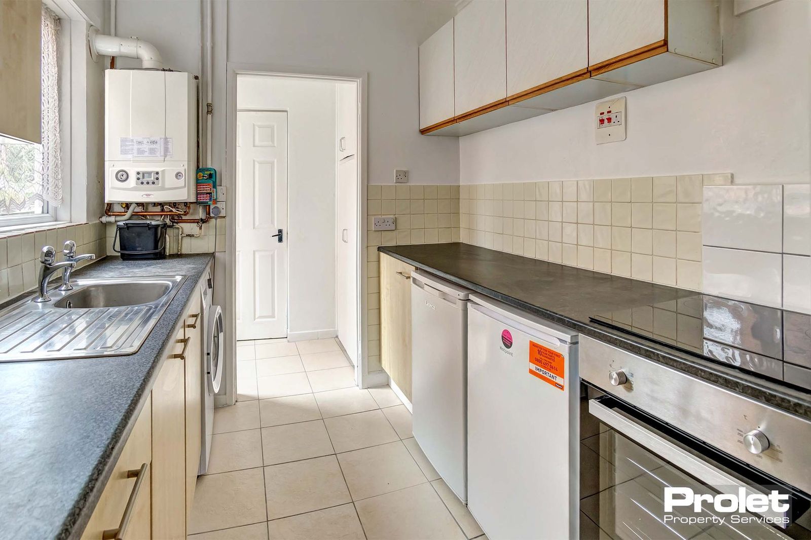 Galley style kitchen with white tiled floor, white fitted units and a dark grey/black worktop.