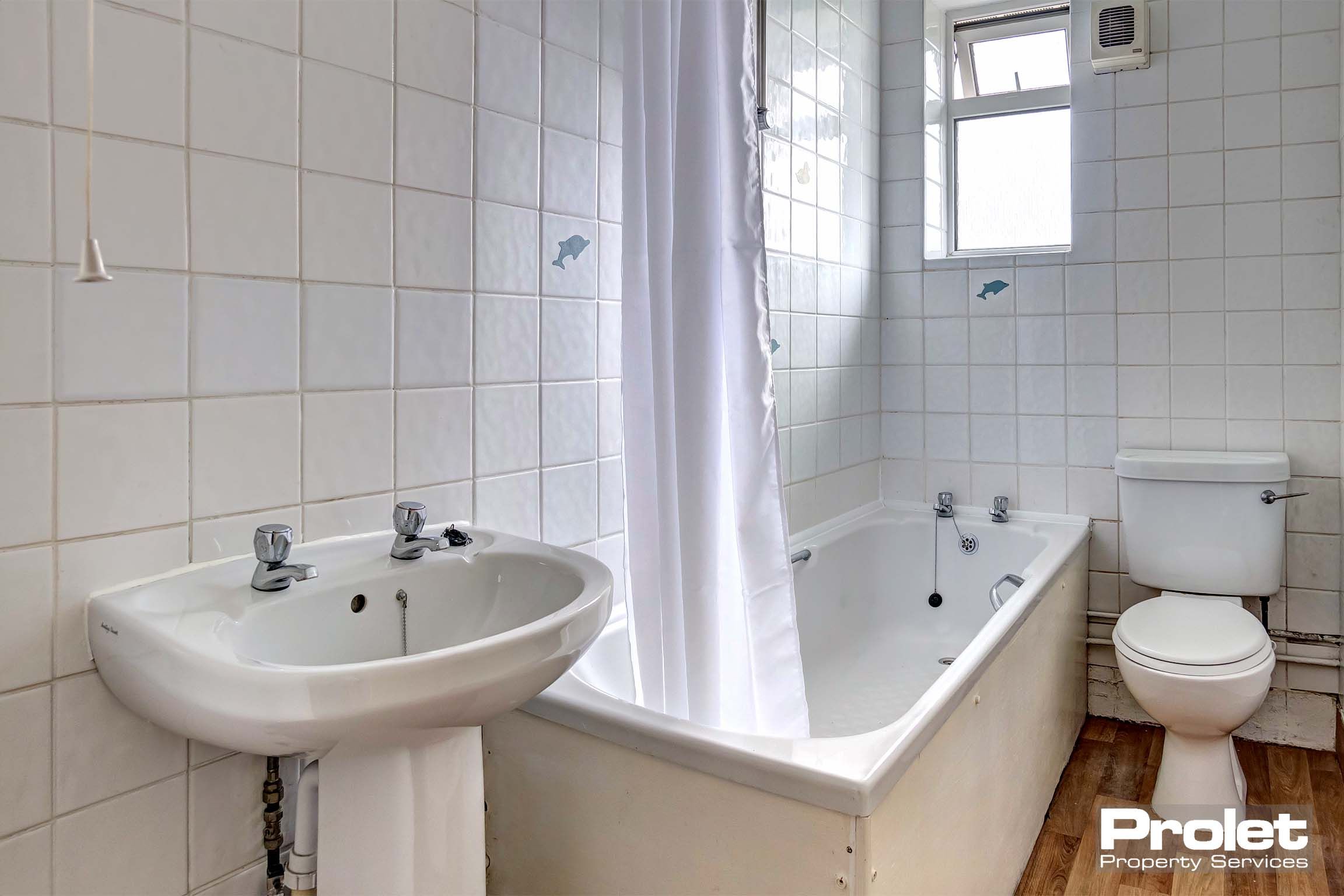 White tiled bathroom with a white sink, bath tub and toilet. A shower over the bath.