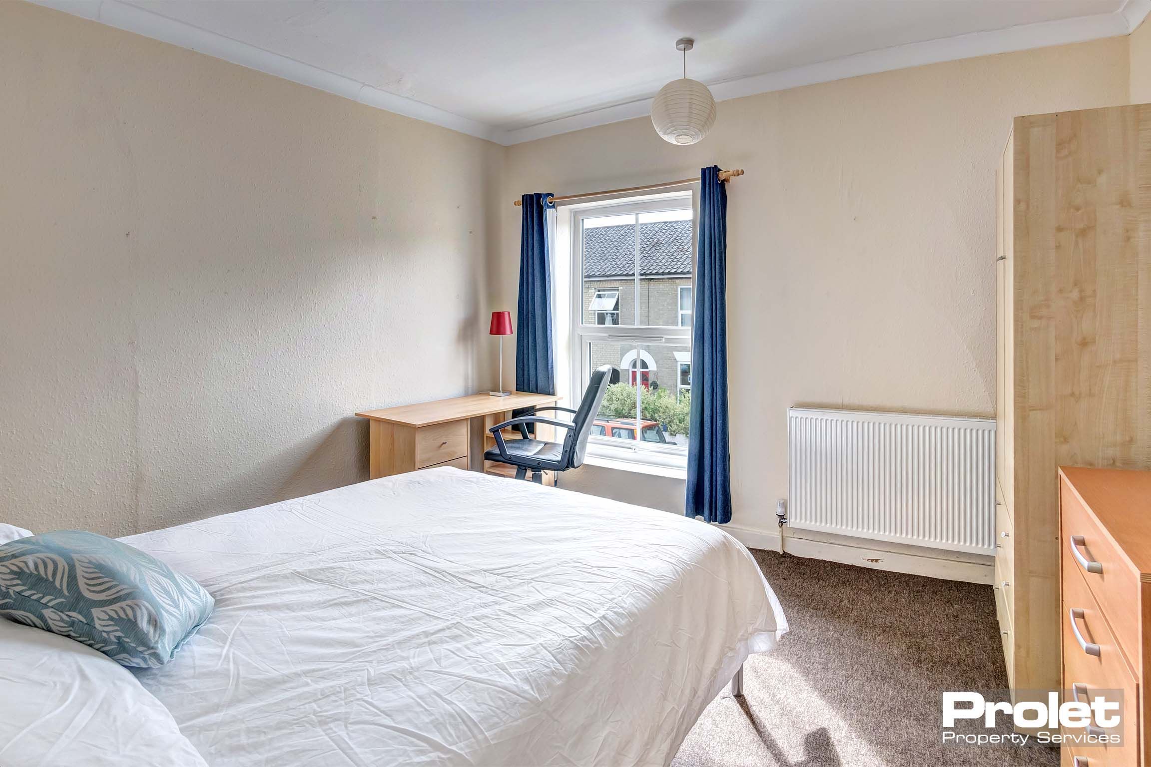 Magnolia painted bedroom with wooden furniture and blue curtains.