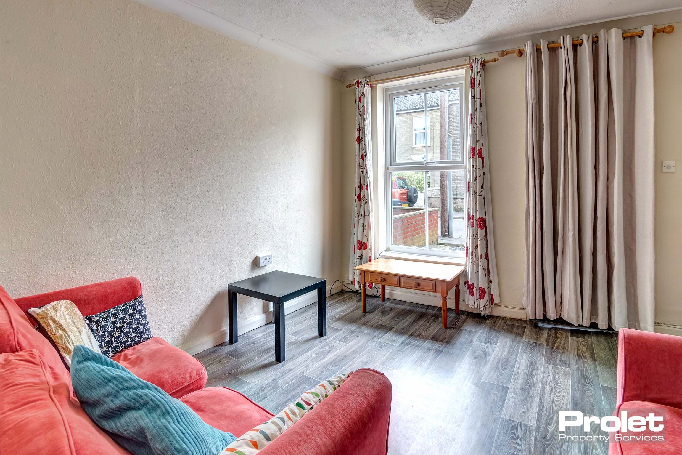 Lounge area with wooden effect lino flooring, two red fabric sofas and a coffee table.
