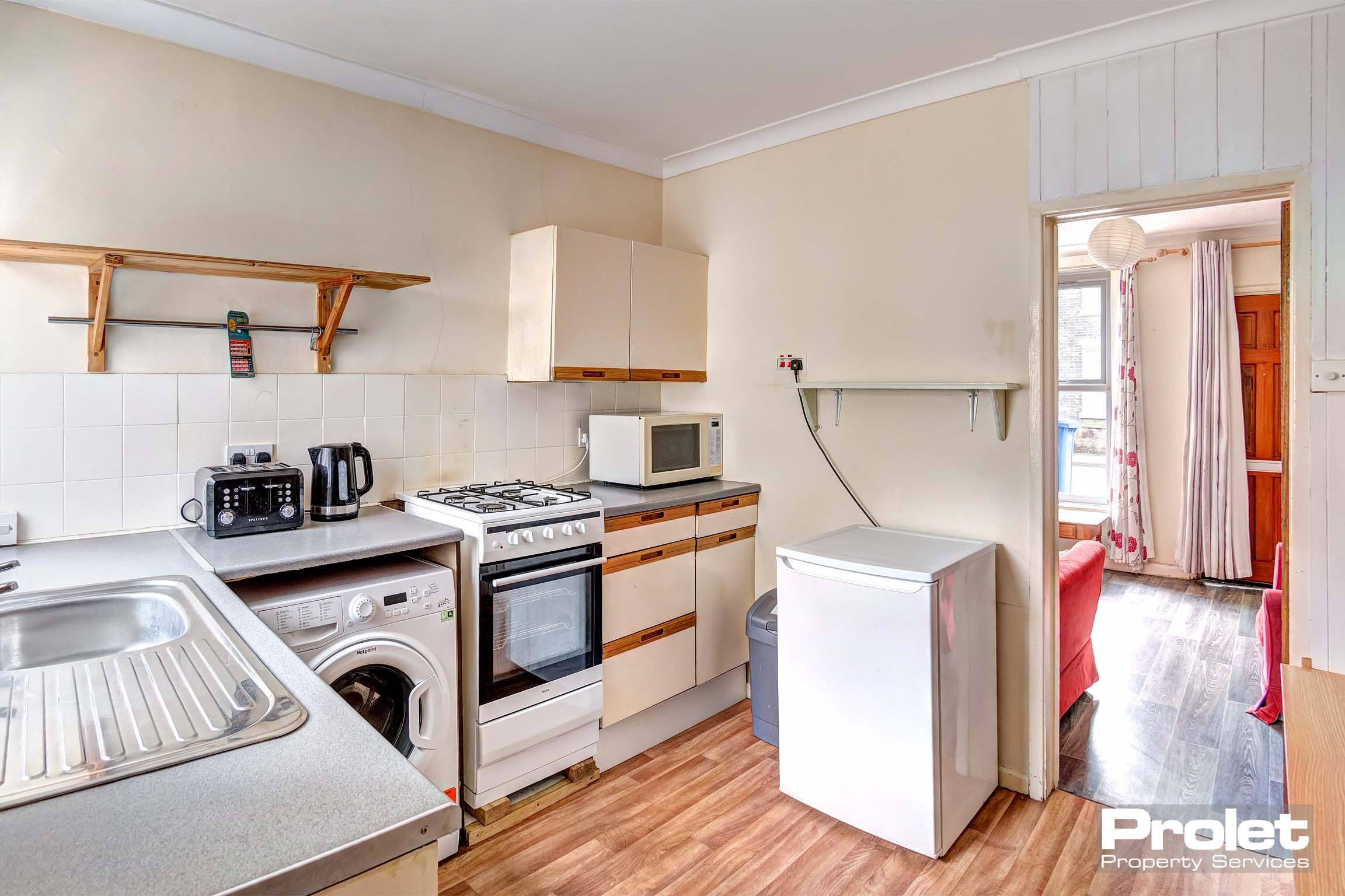 Fitted kitchen with oven, fridge, washing machine and shelf above units for more storage.
