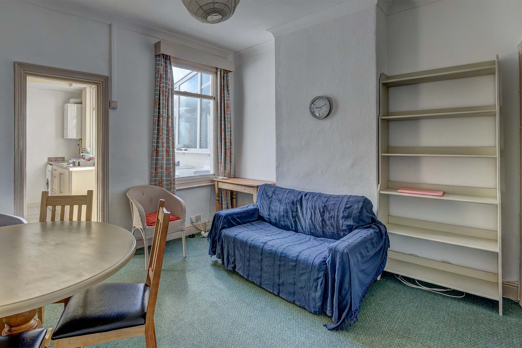 Dining area with wooden bookshelf, blue fabric sofa, dining table with wooden chairs.
