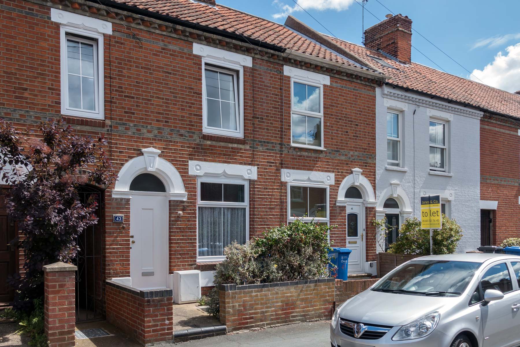 Red brick terraced house with white door.