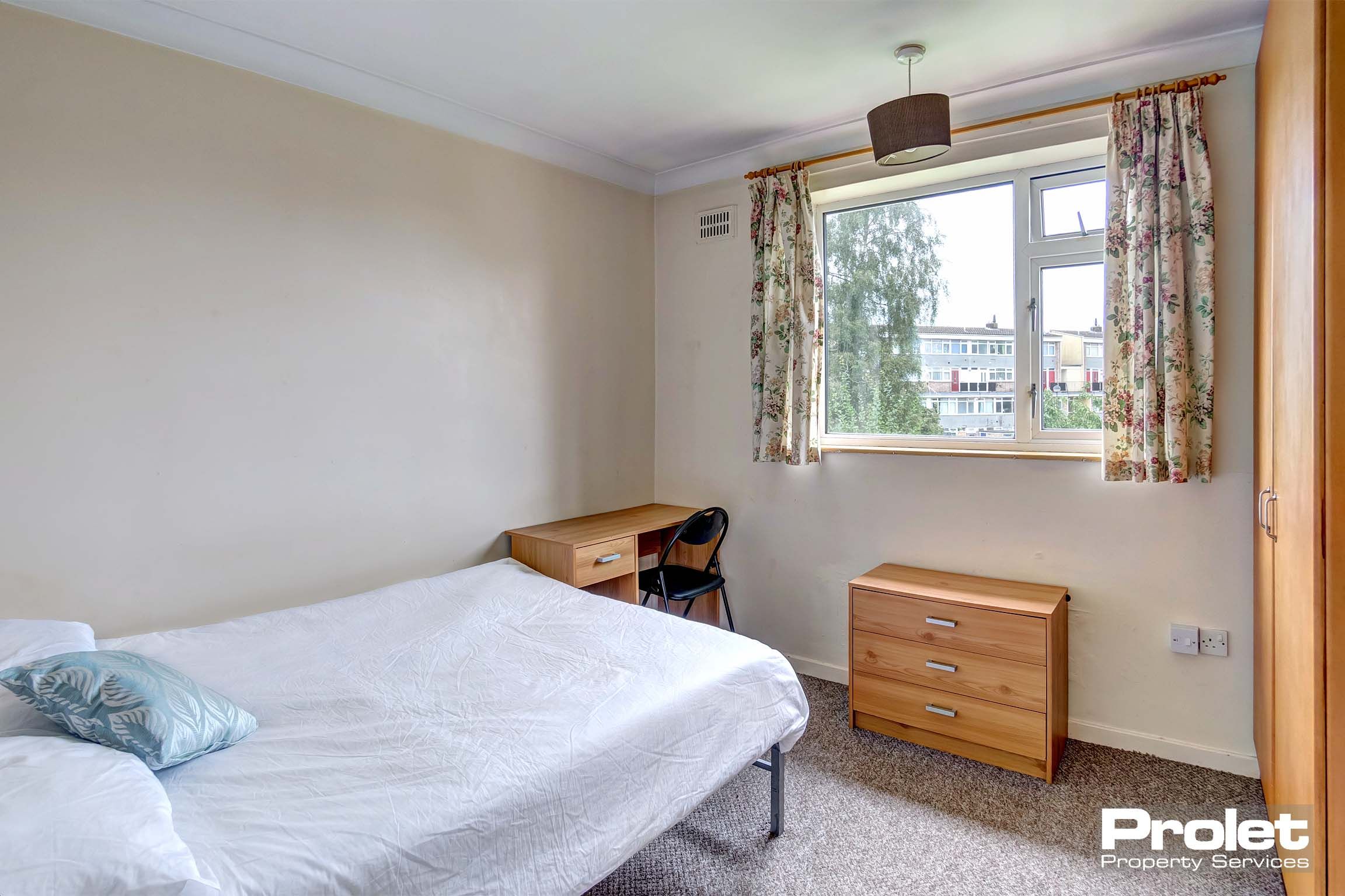 Magnolia painted bedroom with double bed and wooden desk, chest of drawers and wardrobe.