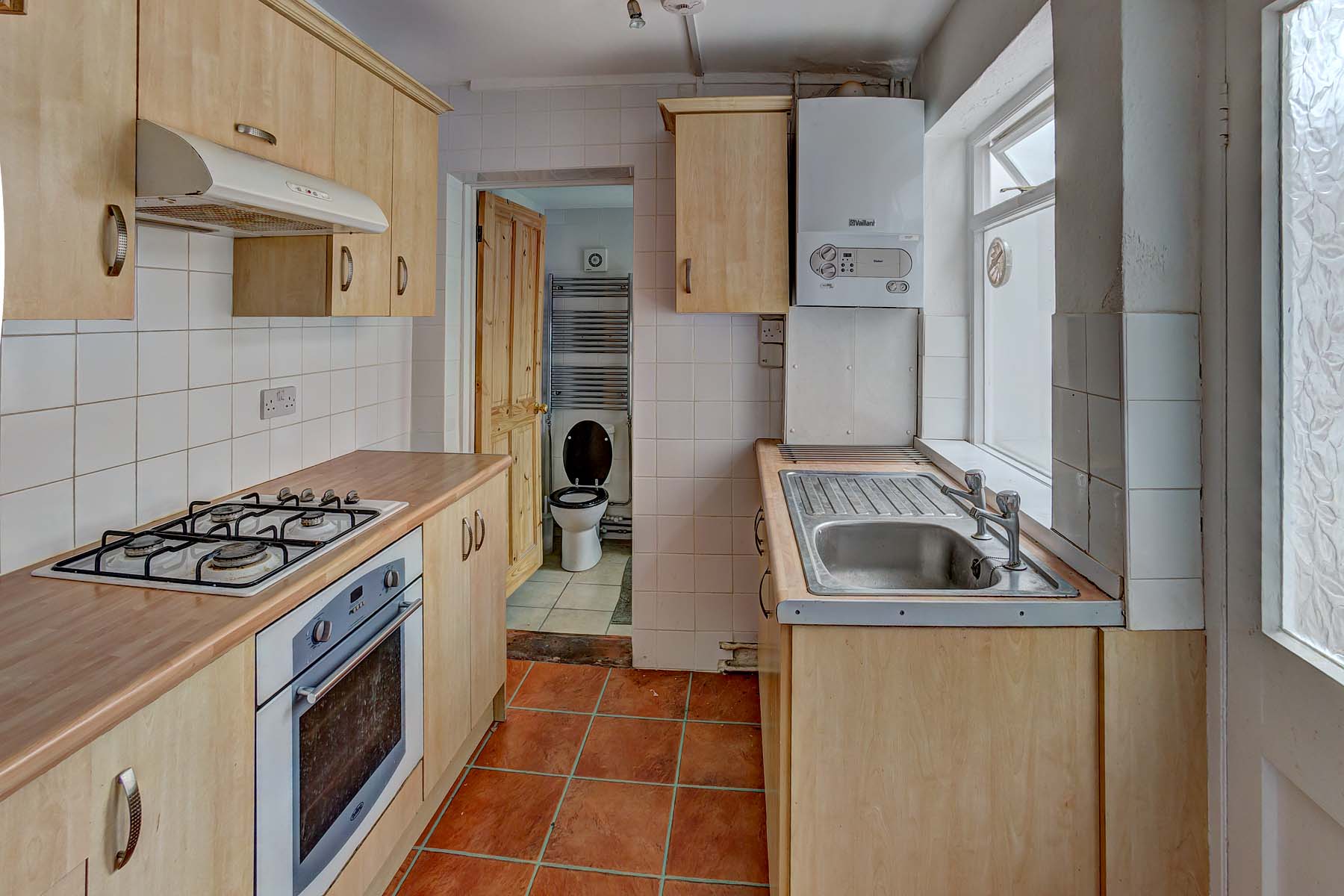 Galley kitchen with wood effect fittings, tiled floor, and large appliances