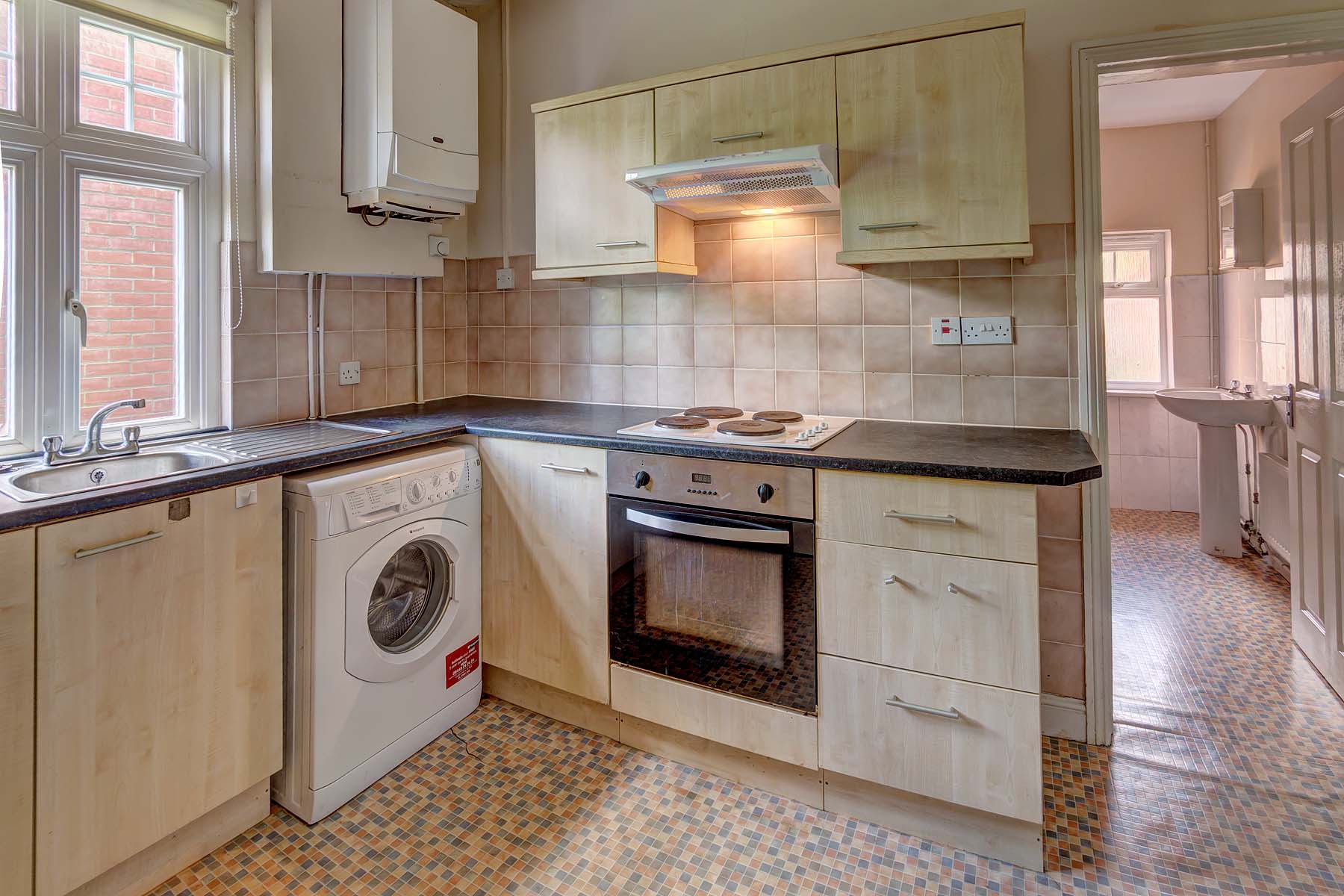 Kitchen with white cabinets, black worktop, and white goods