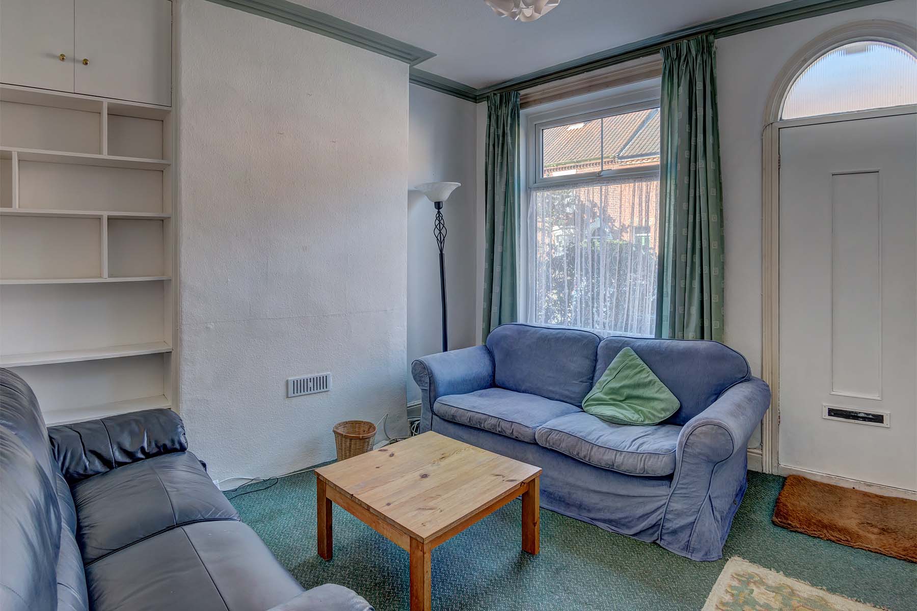 Lounge area with one blue fabric sofa and one black leather sofa, shelving space on the wall and a white front door.
