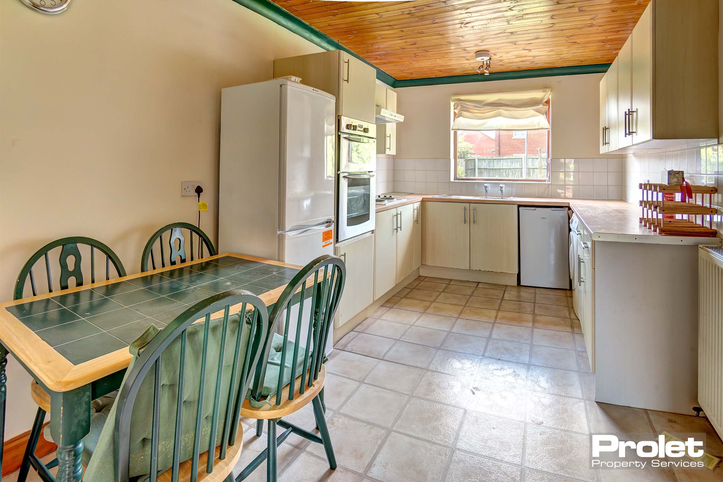 Kitchen with cream cabinets, wood effect worktop, large appliances, and dining set