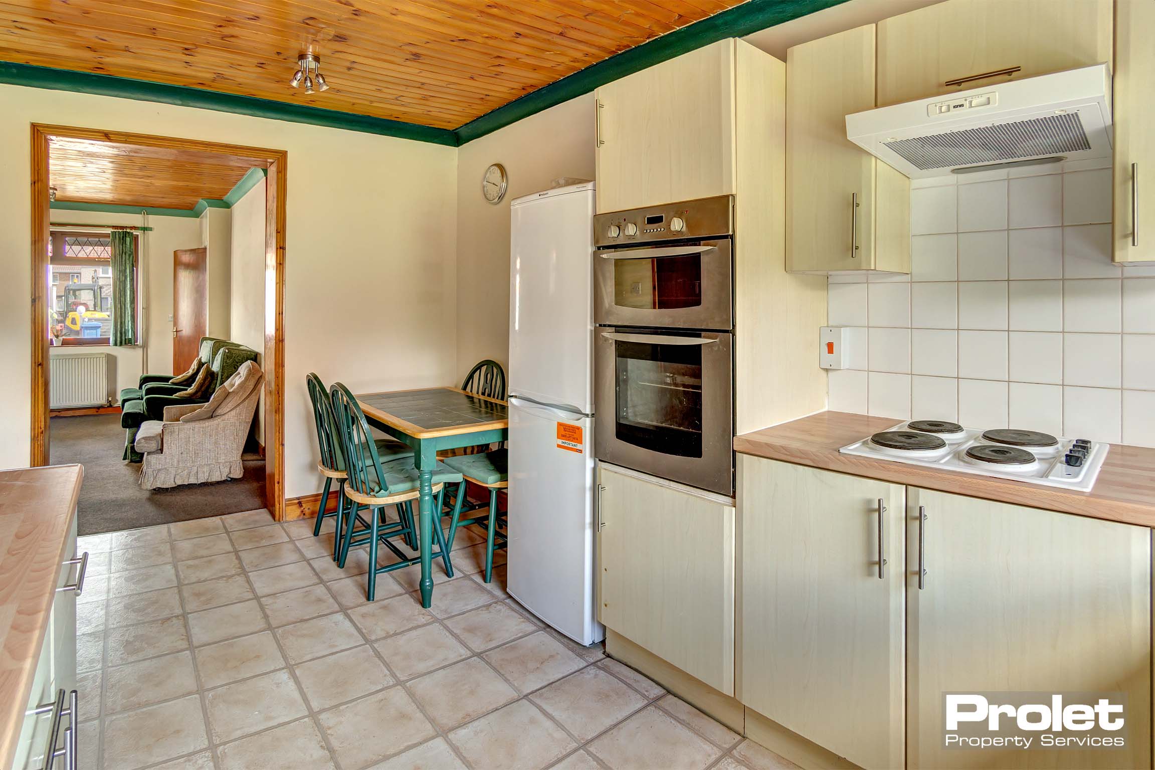 Kitchen with cream cabinets, wood effect worktop, large appliances, and dining set