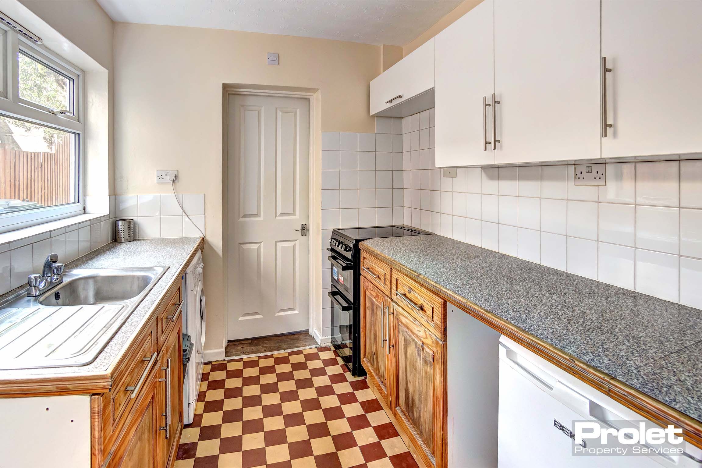 Galley kitchen with tiled floor and white goods