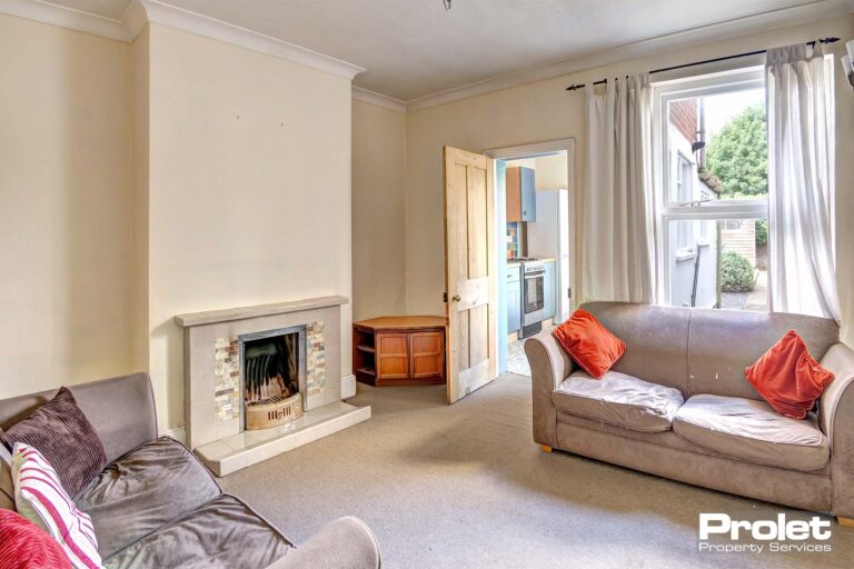 Lounge with cream walls, pale carpet, and sofas, leading to kitchen