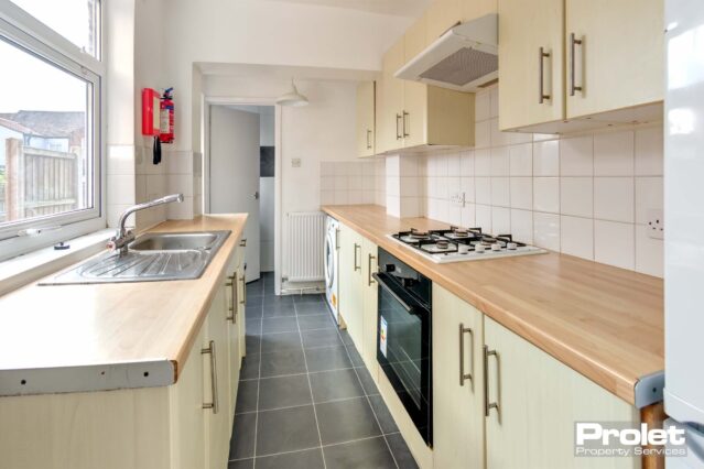 Galley kitchen with cream cupboards, wood effect worktop, and tiled floor.
