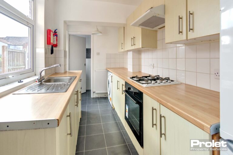 Galley kitchen with cream cupboards, wood effect worktop, and tiled floor.