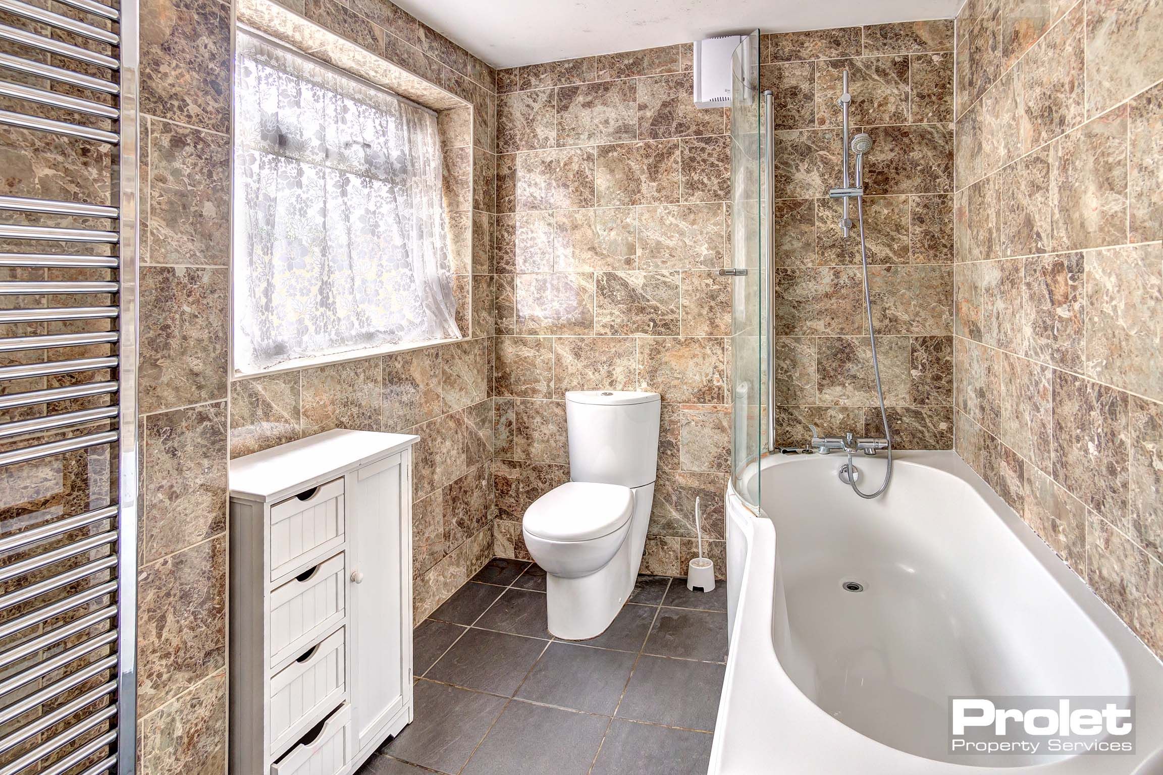 Bathroom with tiled walls and flooring, a white bathtub and toilet.