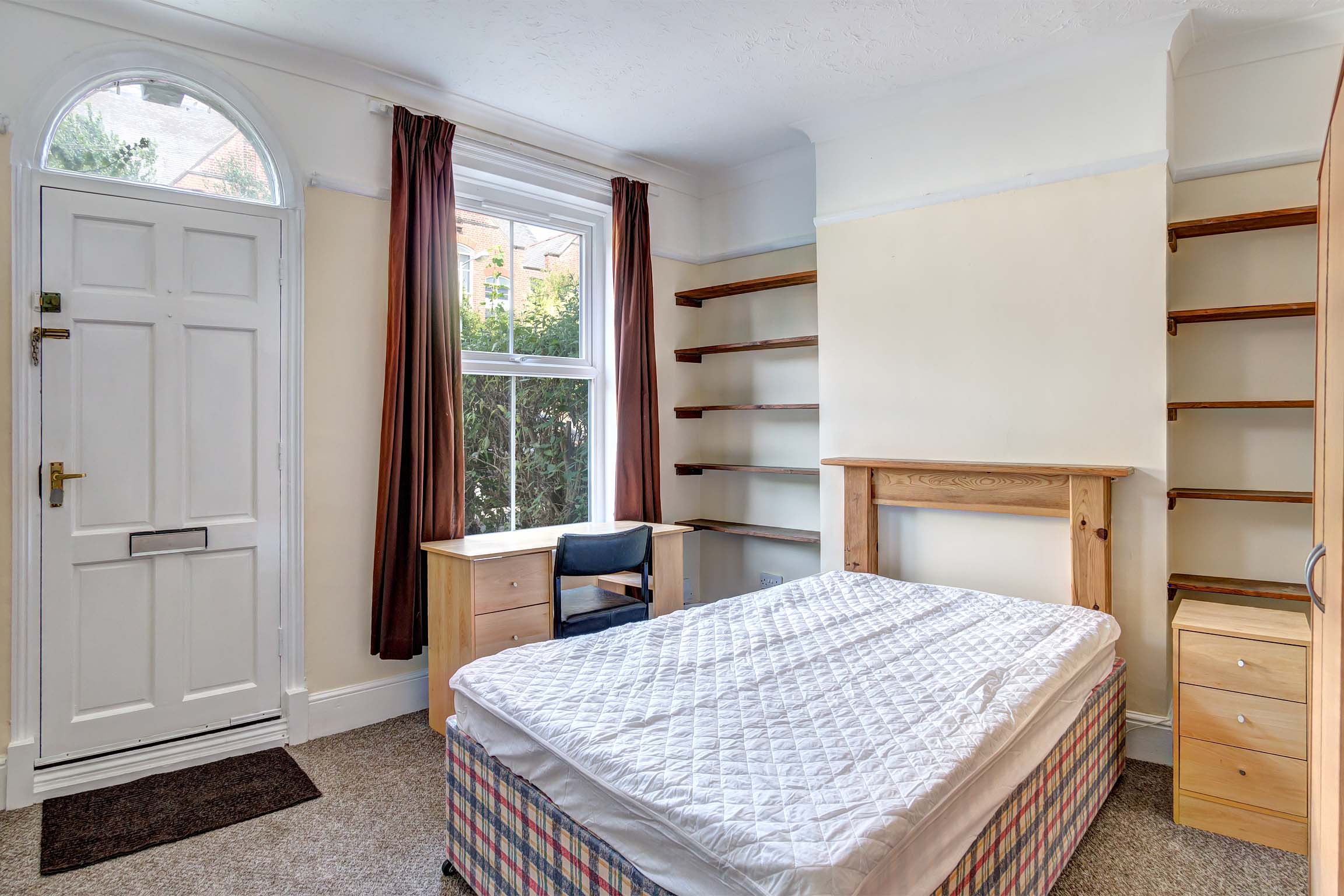 Double bedroom with divan bed base and mattress, built in shelving, a wooden bedside table and desk and front door entry/exit.