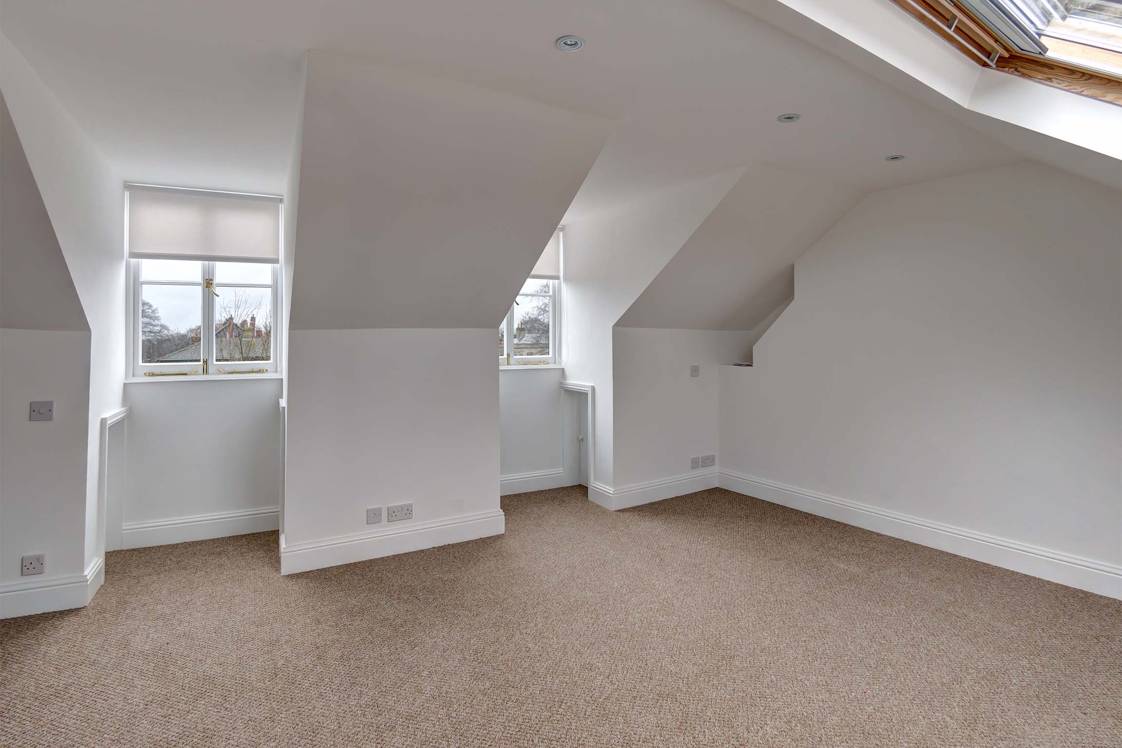 Double bedroom in attic, with velux windows, white walls, and light carpet.