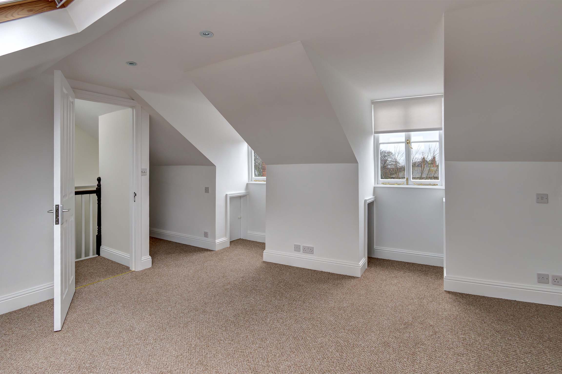 Double bedroom in attic, with velux windows, white walls, and light carpet.