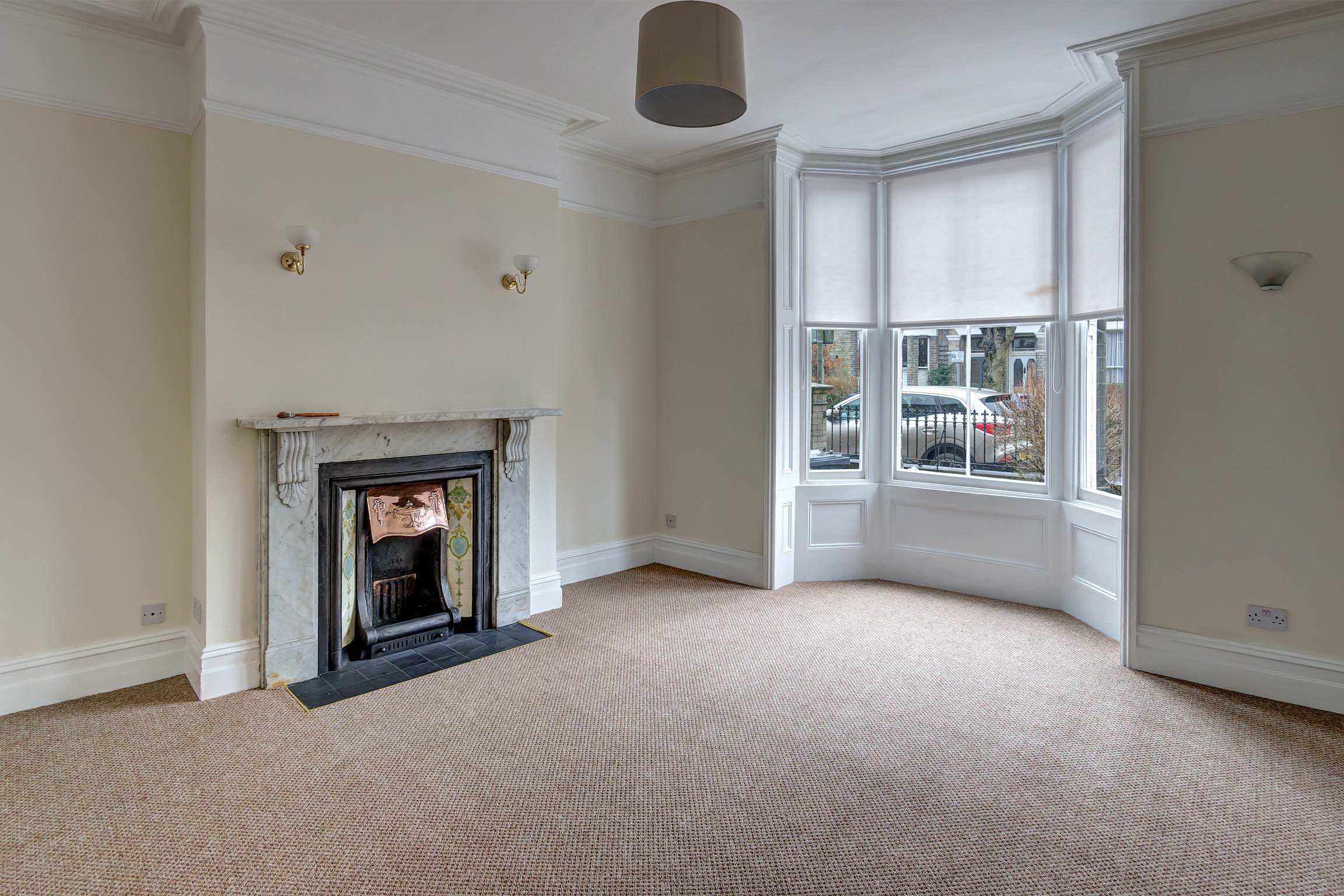 Living room with large bay window and period fireplace. Walls are painted cream with light carpets