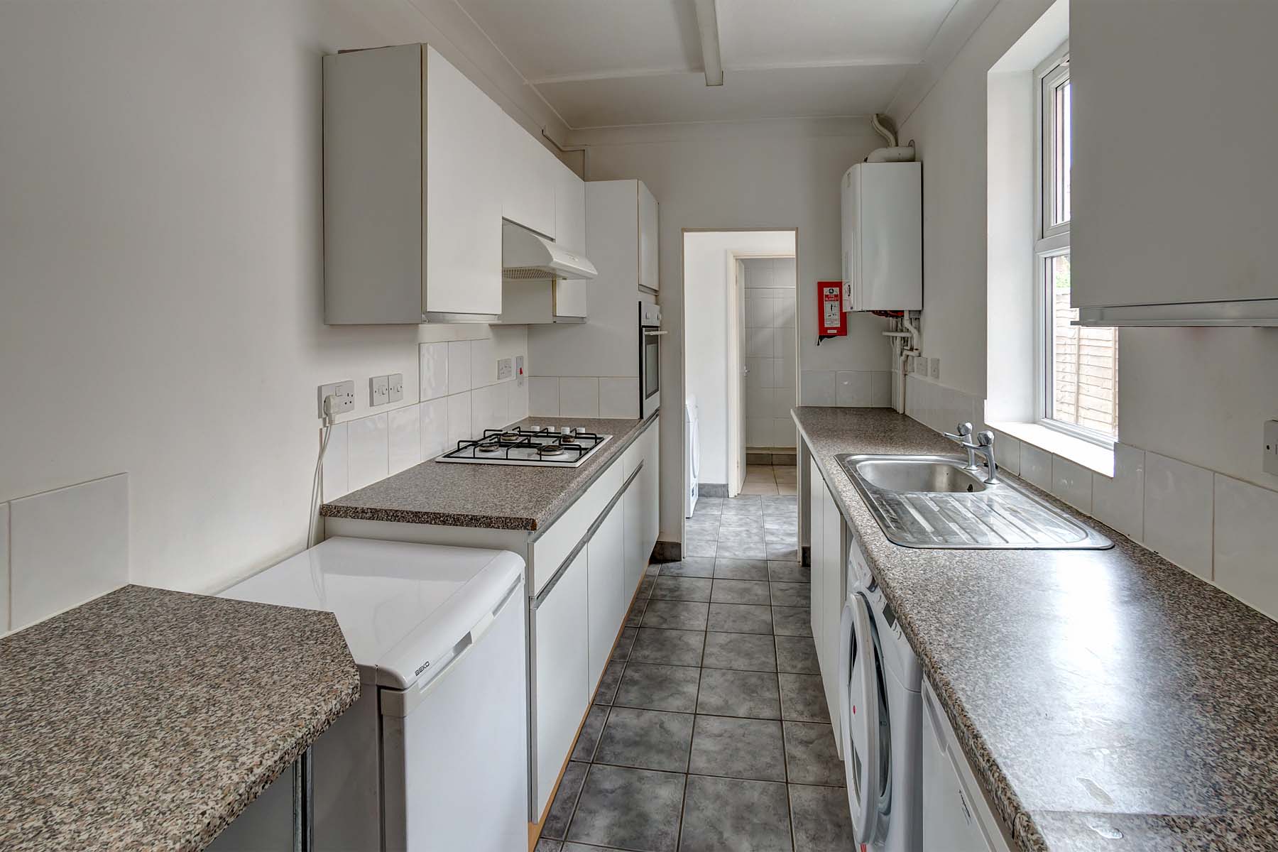 Galley kitchen with white cabinets, grey worktop, tiled floor, and white goods