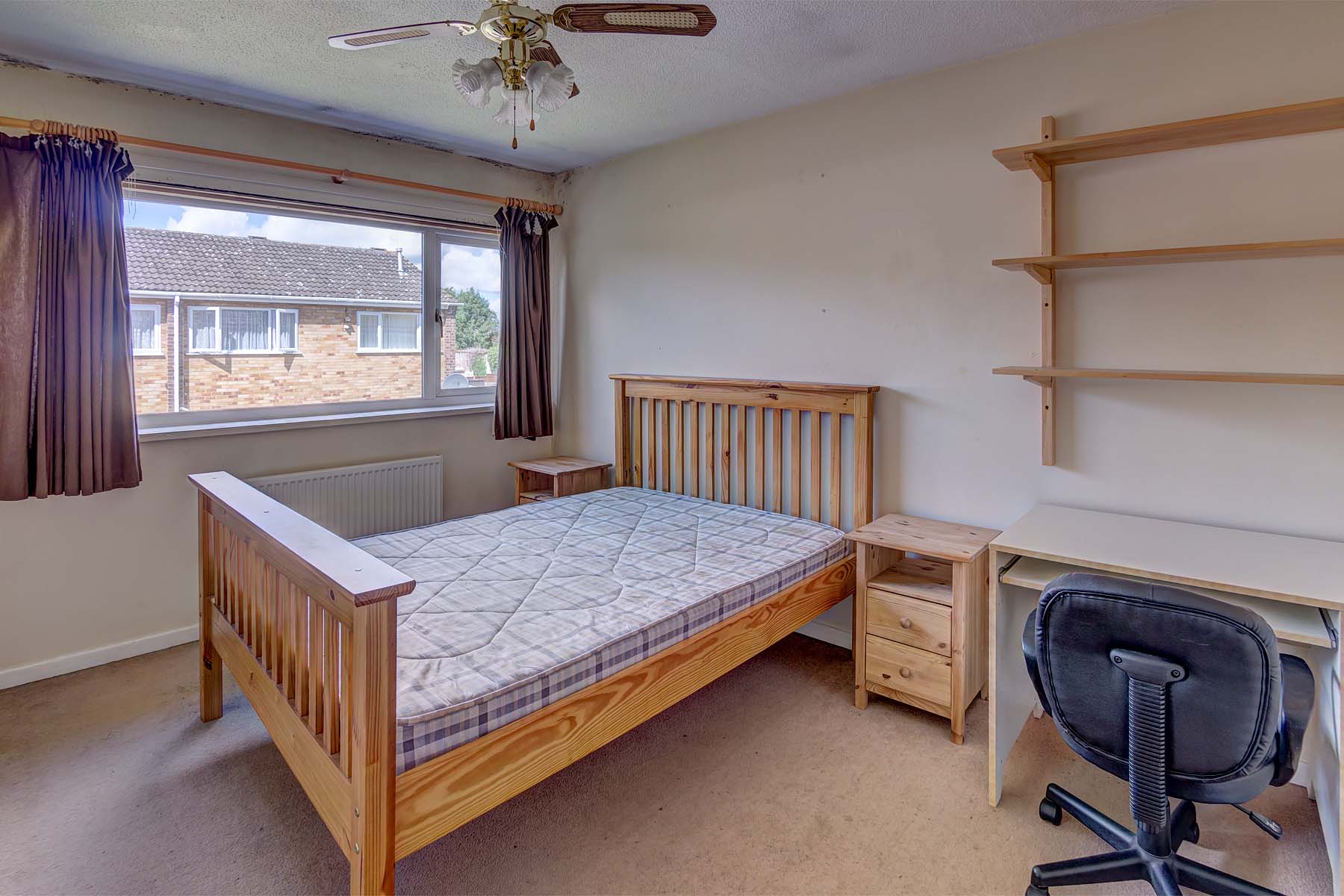 Large bedroom with wooden double bed frame and mattress, shelves on the wall, a wooden bedside table and desk.