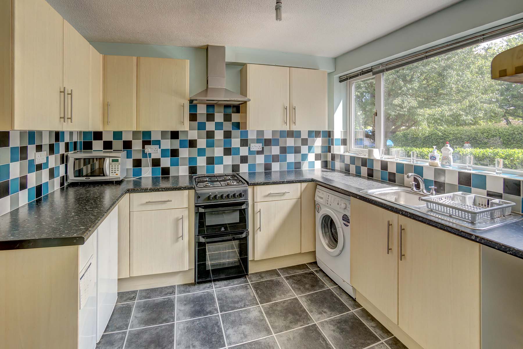 Large fitted kitchen with tiled floor and blue decorative tiled walls. Wooden effect fitted unit and a dark grey/black worktop.