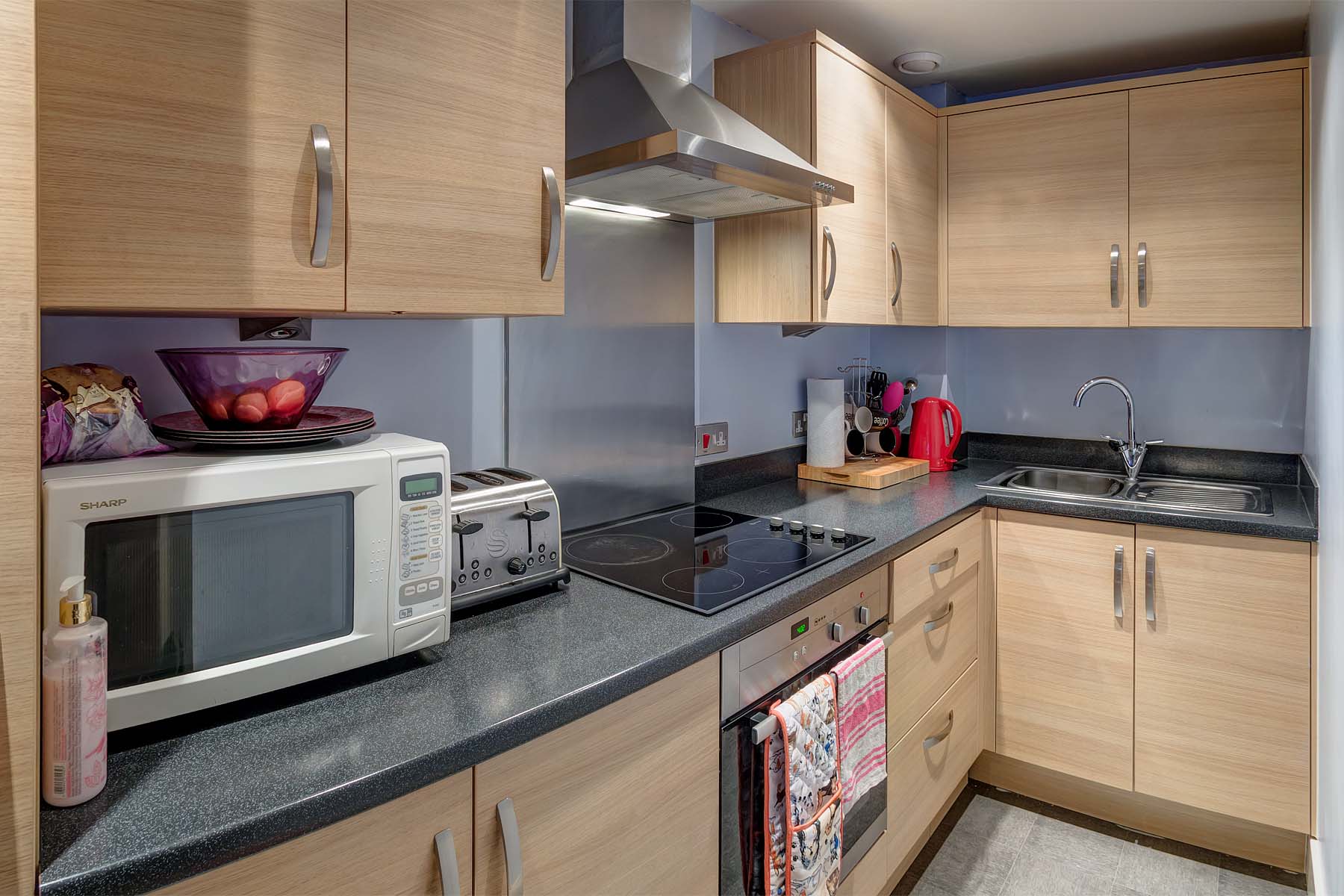 Modern galley kitchen with beech units and black worktops. Oven, hob and integrated fridge freezer. Washer dryer in hallway storage cupboard