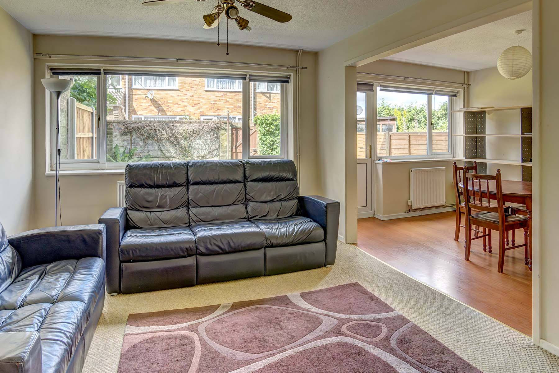 Open plan lounge and dining area with two large black leather sofas and a decorative red rug.