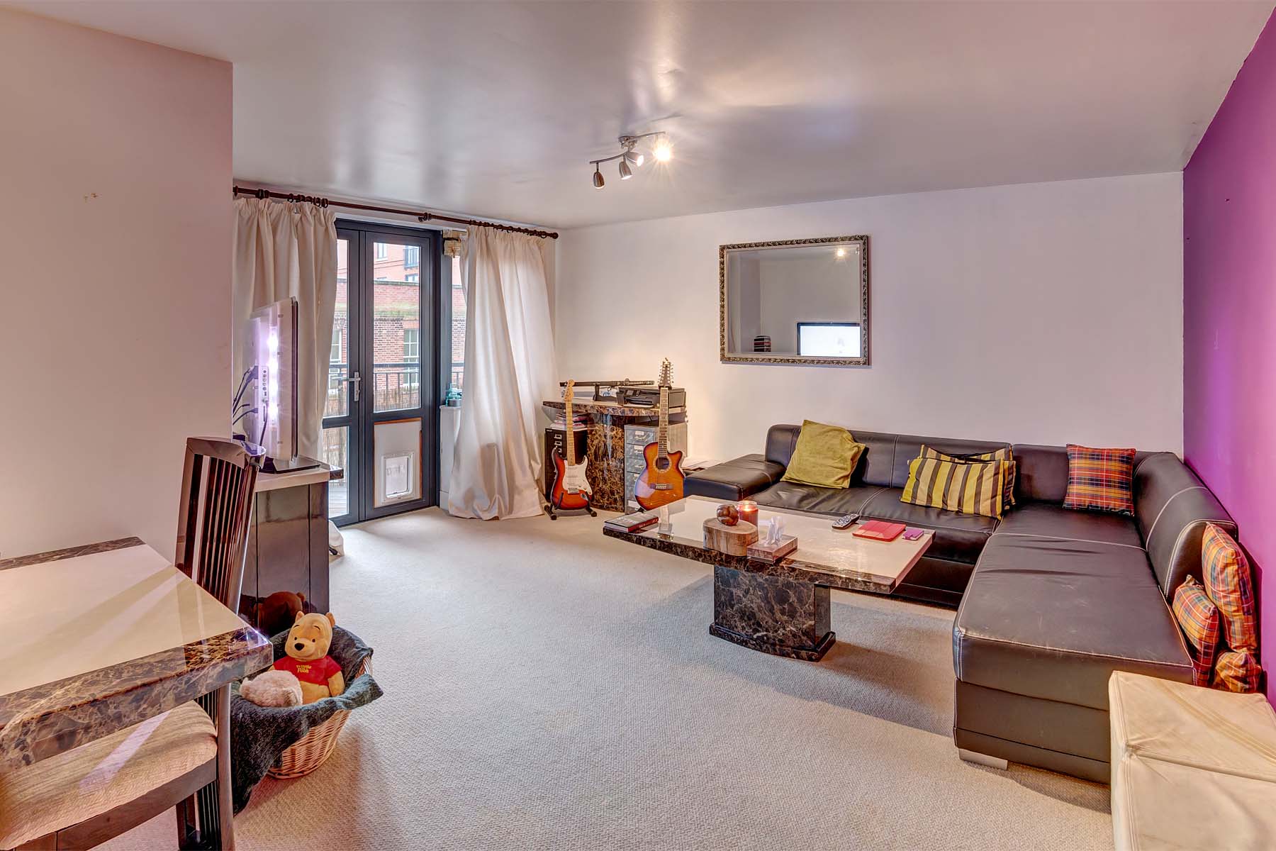 Off white walls with cream carpet, sofa, chair, TV unit and access to external balcony