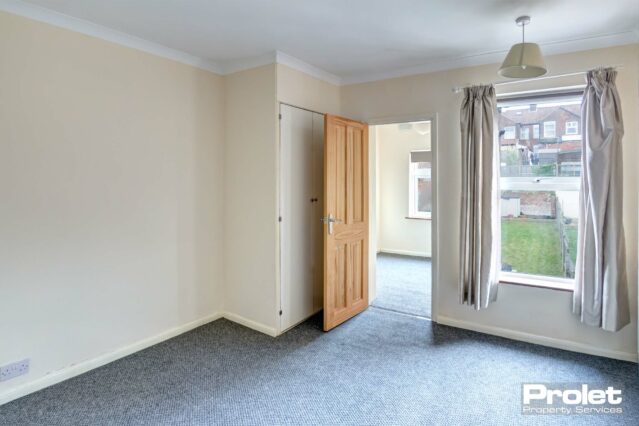 Double bedroom with cream walls and grey carpet, leading to study
