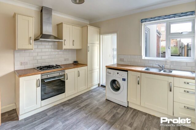 Kitchen with cream cabinets, and wood effect worktops. Oven and washing machine