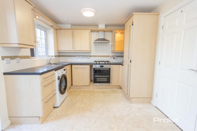 Kitchen with wood effect cabinets, black worktops, washing machine and oven
