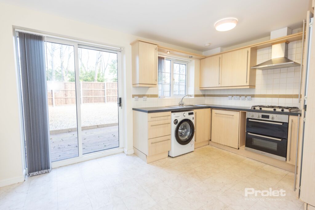 Kitchen with wood effect cabinets, black worktops, washing machine and oven