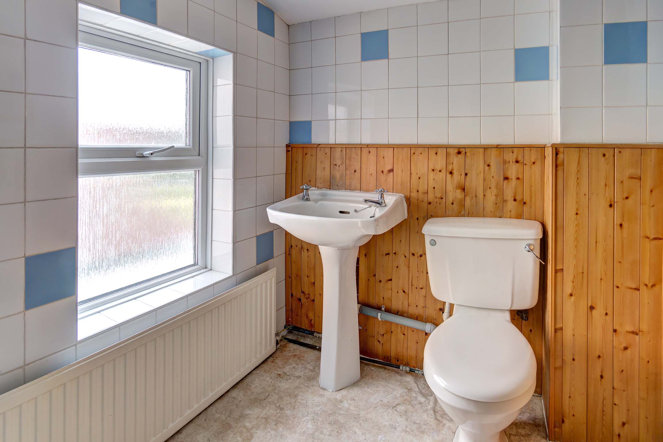 Bathroom with shower cubicle, toilet and sink. Walls half wooden cladding and half tiles white with the occasional blue tile