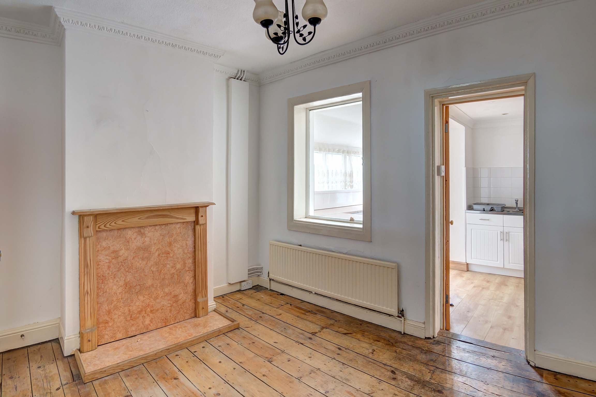 Off white walls with stripped floor boards and fireplace. Glass window looking through to kitchen.