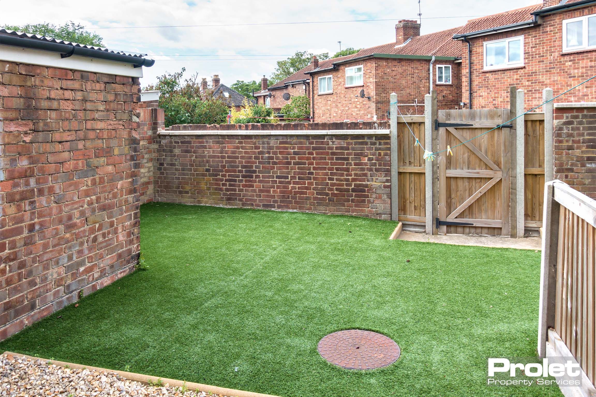 Rear garden with back gate, astro-turf, and small brick outbuilding